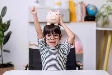 Little Asian girl saving money in a piggy bank, learning about saving, Kid save money for future...