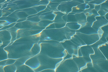 Wunderschöne Muster, die durch die spiegelnde Oberfläche der Wellen in einem Schwimmbecken geformt werden. An kleinen Stellen bilden sich funkelnde Prismen. 