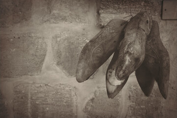 Antique  wooden cobbler  shoe molds needed to make shoes hang on an old stone wall. Shoe Making Repairing