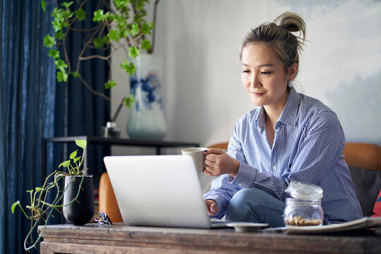 Mature Asian Woman Working From Home Using Notebook Computer