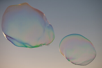 Blowing big soap bubbles in the air against blue cloudy sky. Huge bubble floating in the sky, the sky is bright blue behind, the bubble is transparent but is reflecting colours of the spectrum.