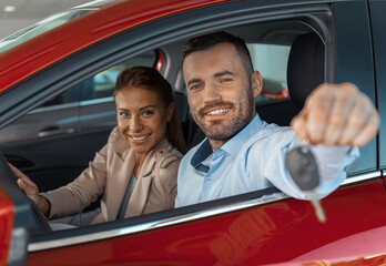 Photo of young couple sitting inside new car. Man showing keys to it. Concept for car rental