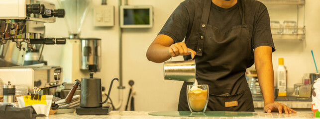 Hand of a female barista gently pouring milk to a cup make hot drink to her customer at a coffee...