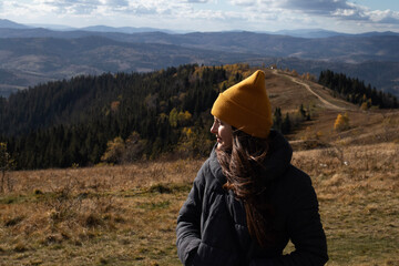 Young happy woman in orange beanie is standing in front of mountains landscape