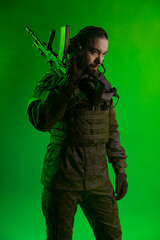 Fototapeta premium soldier in the studio on a green background with colored light. a man in military uniform with a gun, rifle or machine gun. military. airball player