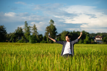 Beautiful dramatic portrait of asian man rural happy farmer standing in the rice field , in a day time summer. Pleased farmer is happily enjoying flourished agricultural crops.