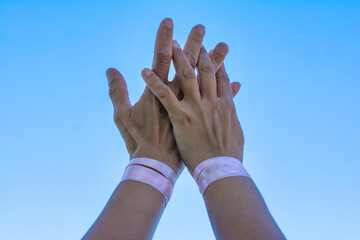 Breast Cancer Awareness Day. Hands of two women with pink ribbon on a blue background. Concept of togetherness and support.