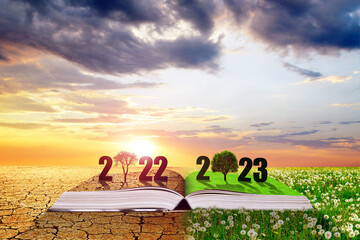 Open book with number 2022 and 2023 at sunset. Dry country with cracked soil and spring meadow with...