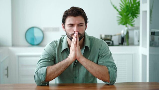 Anxious Caucasian guy, freelancer sitting at the kitchen table in the home interior, experiencing panic attacks and stress due to problems with business, trying get out of a hopeless situation