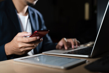 Business man using smart phone, tablet in Dark room. hand holding smart phone , tablet. lap top in front of him.