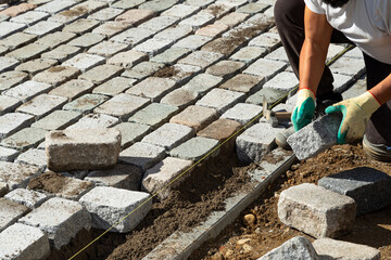 Worker puts paving slabs along the stretched thread on the prepared flat sandy ground on the...