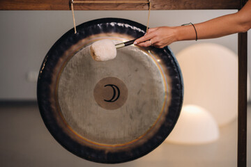 Close-up of a woman's hand pounding a gong with a hammer. Gong and hand beater for gong