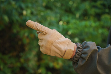 Male caucasian hand in tactical glove over forest background showing gesture points finger. man hand showing different gestures. forefinger. Number one by fingers - obrazy, fototapety, plakaty