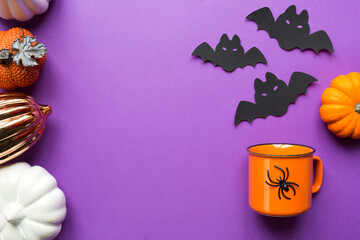 Orange mug on a purple background with terrible Halloween decorations. The concept of the Halloween holiday. Drink, fun, party. Copy space, mock up, flatly