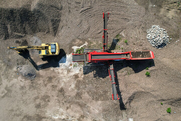 Aerial view above an aggregates manufacturing plant with an excavator working in quarry next to a scalping screen machine for separating mixed materials - obrazy, fototapety, plakaty