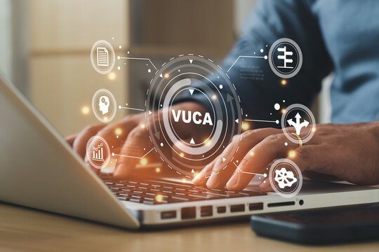 Businessmen using a computer to VUCA text surrounded by volatility, uncertainty, complexity, ambiguity icons. Background, copy space..
