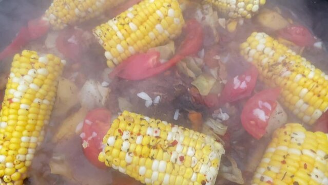 Corn with beef and vegetables. Shurpa in a cauldron. Tomato, red pepper and lamb soup cooked on hot coals. Hot beef hunting goulash or bograch soup with corn cobs, paprika, vegetables and spices.