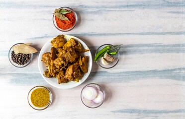 Indian Chicken Gravy or Curry in a White Plate with Green Chilies, Garlic, Ginger, Onion Slices, Black Pepper, Bay Leaf, Red Chili Powder, Dry Curry Leaves and Mustard Sauce in Glass Bowl Isolated
