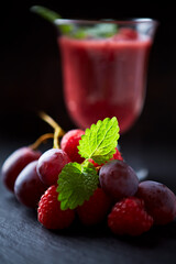 Grapes and raspberries and fresh smoothie in a glass. Dark background. Close up. 