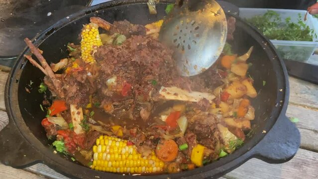 Corn with beef and vegetables. Shurpa in a cauldron. Tomato, red pepper and lamb soup cooked on hot coals. Hot beef hunting goulash or bograch soup with corn cobs, paprika, vegetables and spices.