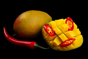 Whole mango, whole chili pepper, sliced hot pepper and cutted half of mango isolated on black...