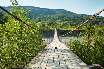 An old wooden suspension bridge on iron cables across a mountain river.
