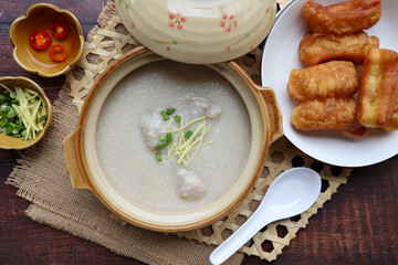 Congee with minced pork in clay pot served with deep fried dough sticks at top view on the wood table - Thai food called Jok Moo