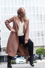 Street photo session of a girl with blond long hair in a beige coat. Photo shoot in the big city.