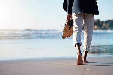 Walking, beach and mental heath with a business man walking in the sand by the sea or ocean after work. Water, nature and freedom with a male employee taking a walk on the coast during summer