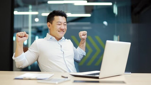 Satisfied Employee with the result successful completion of a project or job. Happy glad Asian office worker business man sitting in office at workplace working on laptop computer. work is done