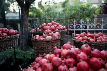 Harvest of ripe pomegranate on dry straw and in wicker baskets at outdoor farmers market in Tbilisi Georgia. Vegetarian healthy food