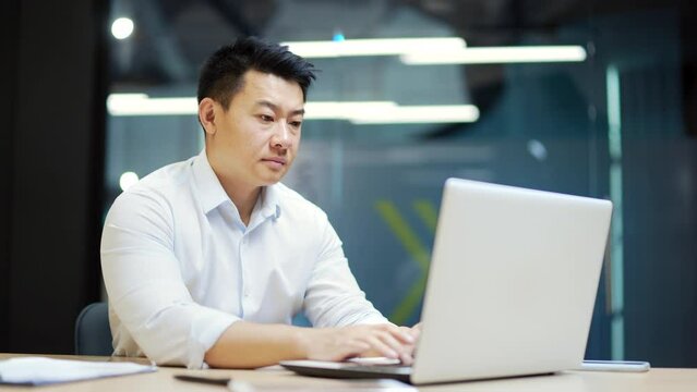Bored asian office worker sitting at work workplace at computer desk leaning on hand. Tired man. Exhausted Businessman employee. Portrait Depressed, unhappy, workless male manager. indoor