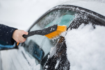 Woman cleaning snow from the car in the winter - obrazy, fototapety, plakaty