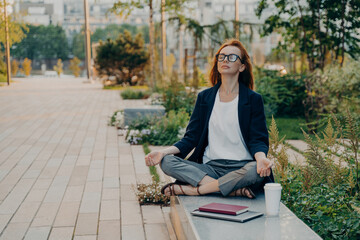 Calm business woman meditating in lotus outdoors, peaceful female freelance employee practicing yoga