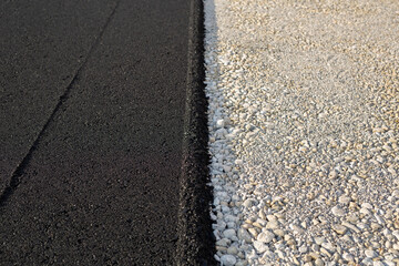New paved road edge and curb. The texture of new asphalt and crushed stone.