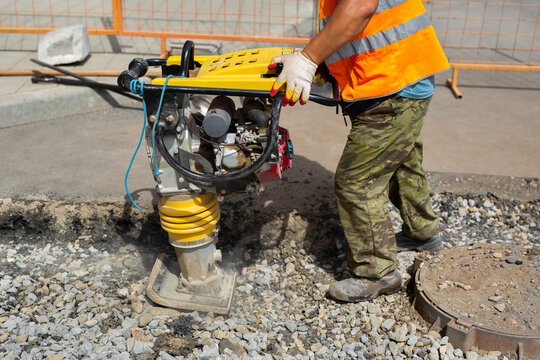 A worker uses a portable vibration rammer during road repairs.