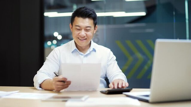 Portrait happy asian guy business men employee reading documents report paper project information letter bank funding notice rejoices feels happiness celebrating triumph sitting font of laptop