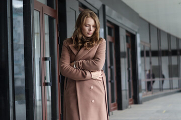Obraz premium Street photo session of a girl with blond long hair in a beige coat. Photo shoot in the big city.