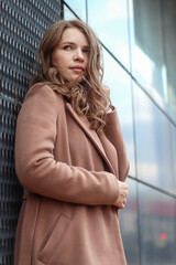 Street photo session of a girl with blond long hair in a beige coat. Photo shoot in the big city.