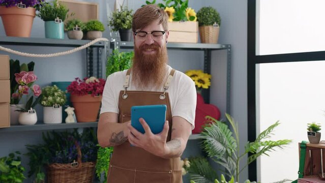 Young redhead man florist smiling confident using touchpad at flower shop