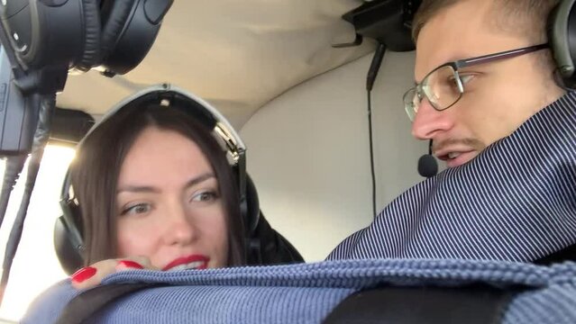 Beautiful couple in a helicopter while flying over the city. The young man shows the woman with the red lips a view of the city.