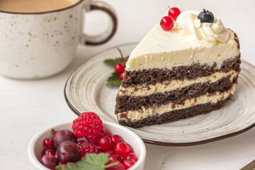Delicious berry cake. A layered cake with white cream on the plate, a white ceramic cup, a bowl of red berries on white table