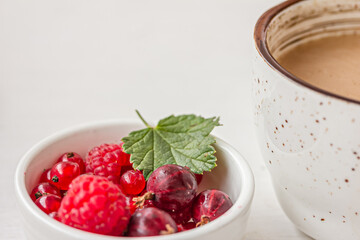 A bowl of red berries a white ceramic cup of coffee on white table, mock up, copy space