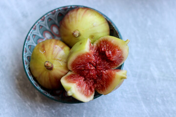 Fresh figs in a ceramic bowl. Red fruit flesh close up photo. Grey background with copy space. Natural vitamins and antioxidants. Eating fresh concept. 