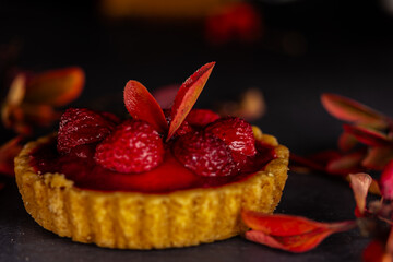 Autumn dessert. A piece of berry cake, tartlet shell with berries, right colored autumn leaves, on dark background.