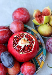 Fresh Mediterranean fruit on a blue ceramic plate. Colorful still life with pomegranate, figs, plums. Healthy eating concept. 