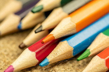 Several colored pencils of different colors on a background of coarse burlap. Close-up, selective focus.