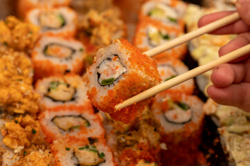 Someone takes a chopsticks roll from a set of different types of rolls in a box.