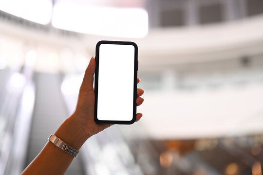Cropped image of woman hand holding smart phone against blurred escalator background. Empty screen for your advertise text