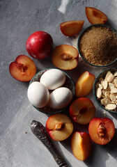 Plum pie in process. Fresh ingredients on a table. Top view photo of plums, almonds, demerara sugar, eggs. Sweet cake ingredients closes up. 